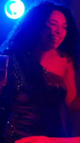 Vertikales-Video-Von-Zwei-Frauen,-Die-In-Einem-Nachtclub-Oder-Einer-Bar-Tanzen-Und-Alkohol-Trinken,-Mit-Funkelnden-Lichtern-Im-Hintergrund